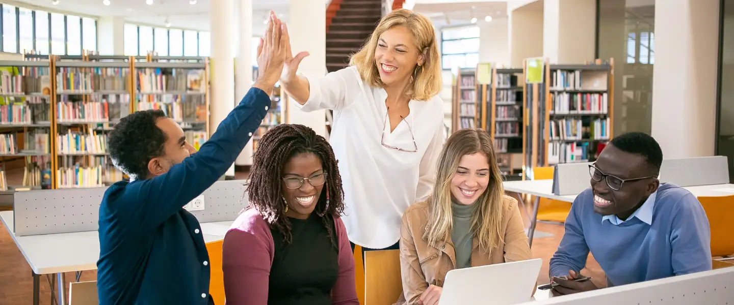Un groupe d'apprenants souriants échangeant avec leur formatrice dans un espace lumineux, symbolisant une communauté d'apprentissage bienveillante et ouverte.
