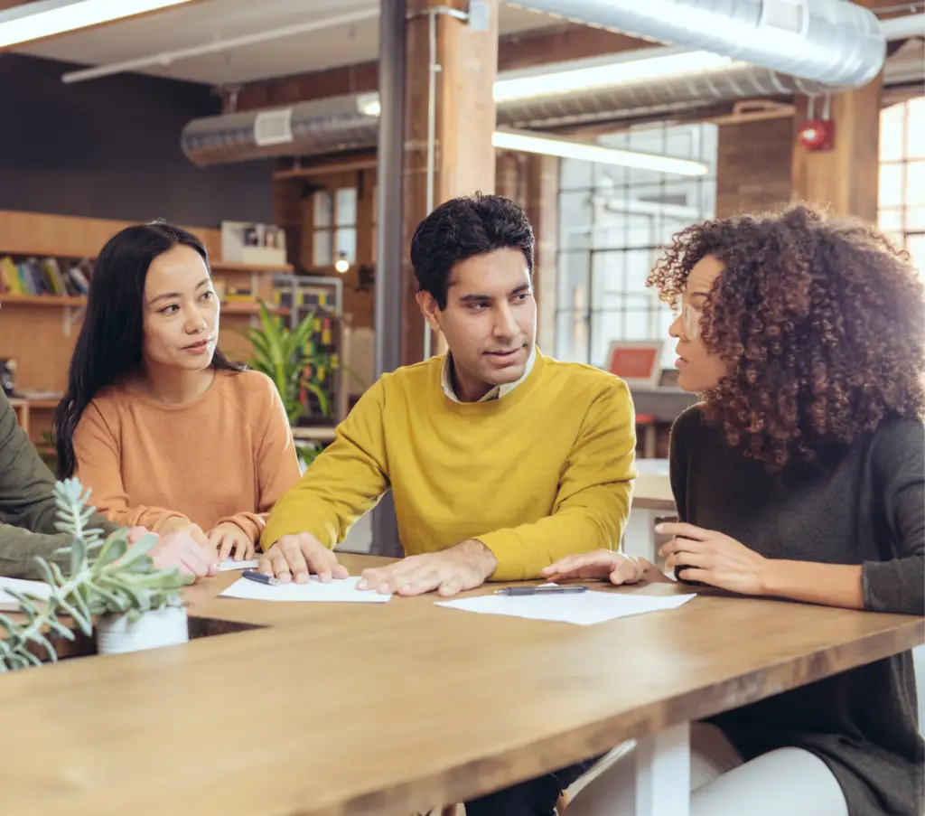 Un groupe diversifié de jeunes adultes discutant avec sourire et attention autour d'une table, illustrant le partage et l'échange lors d'un cours de langue.